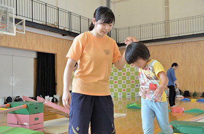 写真：遊具で遊ぶ子どもの手を引いて、安全に配慮しながら遊ばせる学生