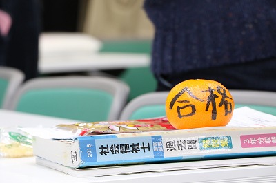 写真：合格と書かれたみかんが、社会福祉士国家試験の参考書の上に載っている
