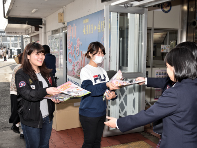 写真：高校生2人にチラシを渡す学生2人