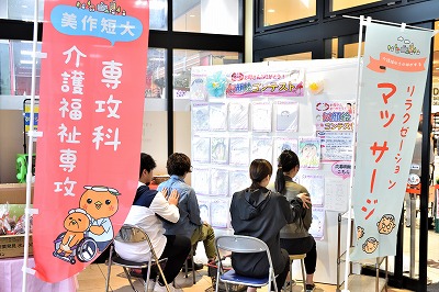 写真：リラクゼーションの場を提供。学生2人が買い物客2人にリラクゼーションマッサージを実施する様子