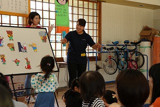 写真：児童館でホワイトボードシアターを行う学生と、それを見る親子