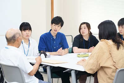 写真：学生グループのグループワークに参加しする町内会住民。その住民を囲んで話をする学生