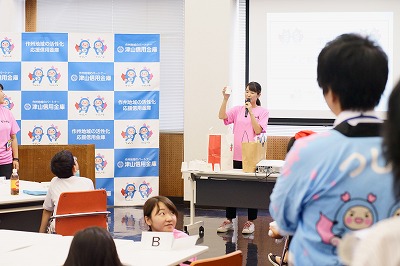 写真：手作り貯金箱の材料の説明をする学生