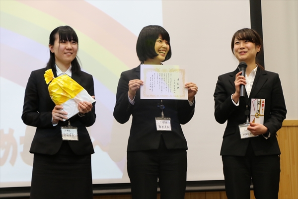 写真:表彰式で、表彰状と記念品をみんなに見せる3名の学生