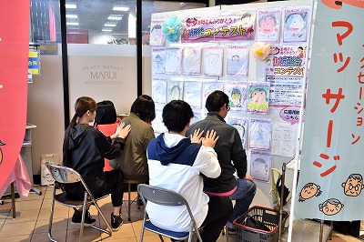 写真：リラクゼーションの場を提供。学生2人が買い物客2人にリラクゼーションマッサージを実施する様子