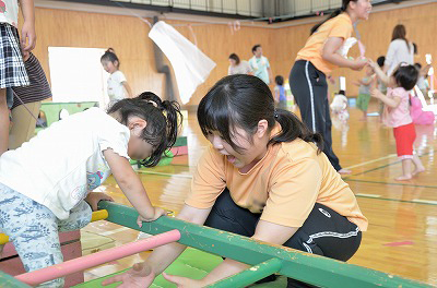 写真：はしご型の遊具で遊ぶ子どもを、はしごをまたぐことができるように誘導する学生