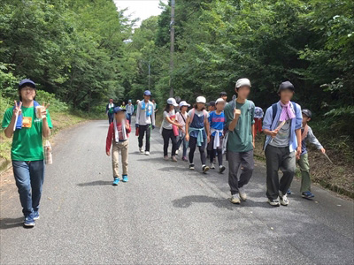 写真：木に囲まれた道を楽しそうに歩く学生と小学生