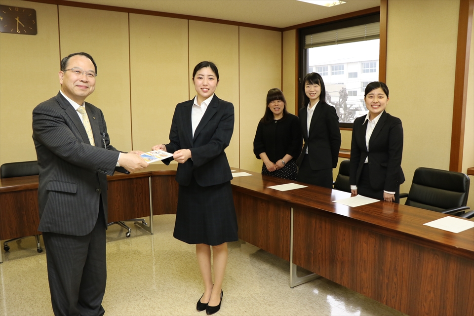 写真：1名の学生がガイドを市の職員に手渡す様子