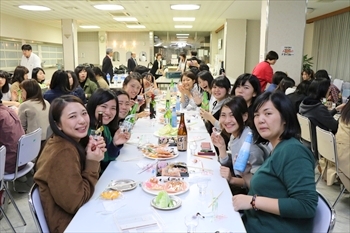 写真：机を囲んで、日本酒を飲みながら食事をするたくさんの学生