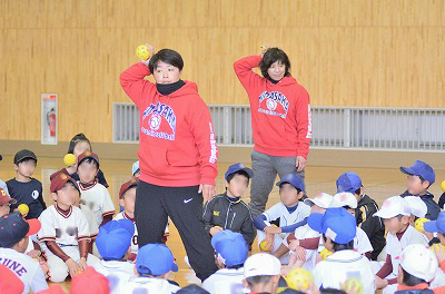 写真：体育館内では小学校低学年の受講者にボールを投げるポイントを説明するひろせ選手と伊藤選手