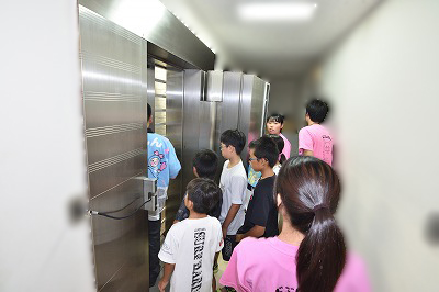 写真：貸金庫の前で貸金庫について話を聞く子どもたちと学生