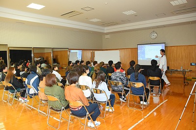 写真：セミナーの様子。熱心に話をする講師。参加した学生も熱心に聞き入る様子。全体を後ろから撮影した写真