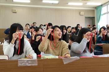 写真：ひもを使ったマジックをやってみる3名の学生
