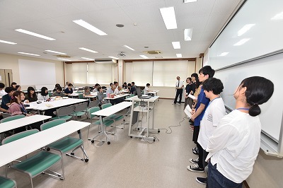 写真：アンケート調査の発表を行う学生グループ1組。それを聞く学生と町内会の住民