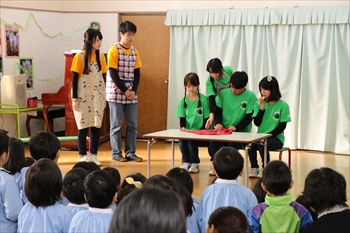 写真：お菓子を食べる演技をする子ども役の学生と、それを見る母親役の学生