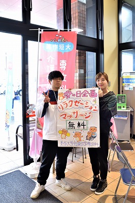 写真：企画を説明したパネルを持ってアピールする学生2人