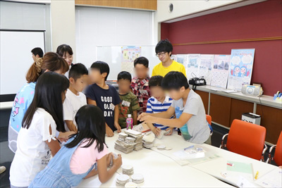 写真：コインタワーゲームをする小学生とそれを見守る大学生