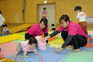 写真：はいはいする子どもとそれを見守る学生