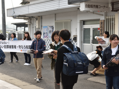 写真：横断幕の前でチラシを配る学生3人