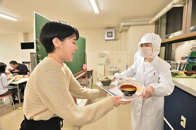 写真：完成した食事を受け取る学生と手渡す担当学生