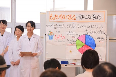 白衣を着た学生が講義をする様子