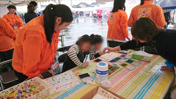 写真：野菜のはんこを紙に押す2名の子どもと見守る学生