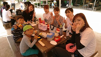 外で子供たちと学生がお弁当を食べている姿