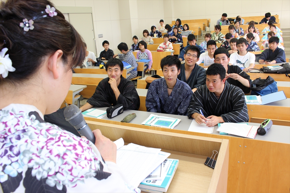 写真：浴衣を着て教壇に立つ先生の後ろ姿、椅子に座って授業を受ける学生