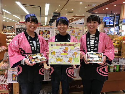 写真：両三柳店の販売ブースを前に記念撮影