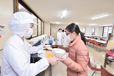 写真：完成した献立を提供する学生。受け取る学生