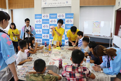 写真：財布に作り方を説明する学生とそれを聞く小学生