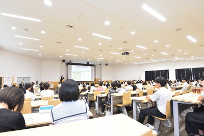 写真：全体会で大学の概要説明をする広報主幹の教員