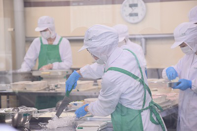 写真：調理担当の学生の丁寧に盛り付けをする様子。