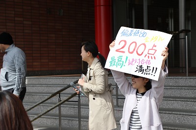 写真：偏差値80、200点、最高!、絶対合格、満点!と書かれたプラカードを掲げる教員