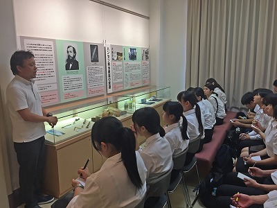 写真：歴史館内で展示資料や歴史について話を聞く。メモを取る学生