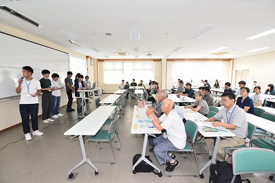 写真：アンケート調査の発表を行う学生グループ1組。それを聞く学生と町内会の住民