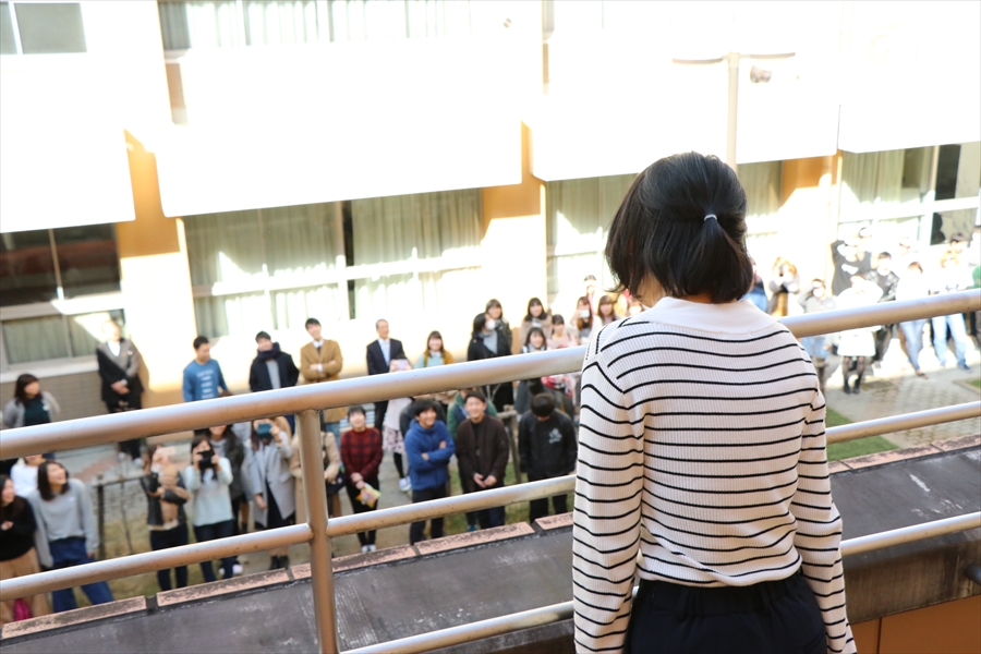 写真：2階のベランダから1階に向かって叫ぶ1名の女子学生