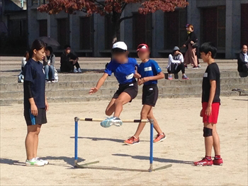 写真：ハードルを飛ぶ小学生とそれを指導する陸上部員