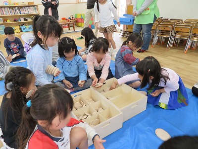 写真：木製石ころ積み木が入った箱を囲んで、思い思いに積み木を手に取る子どもたち