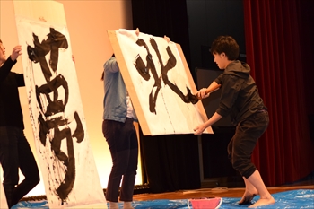 写真：書道パフォーマンスで「北」を大きな紙に書く1名の学生