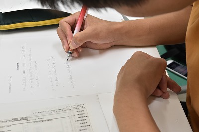 写真：ノートにメモを取る学生の姿。手元アップ
