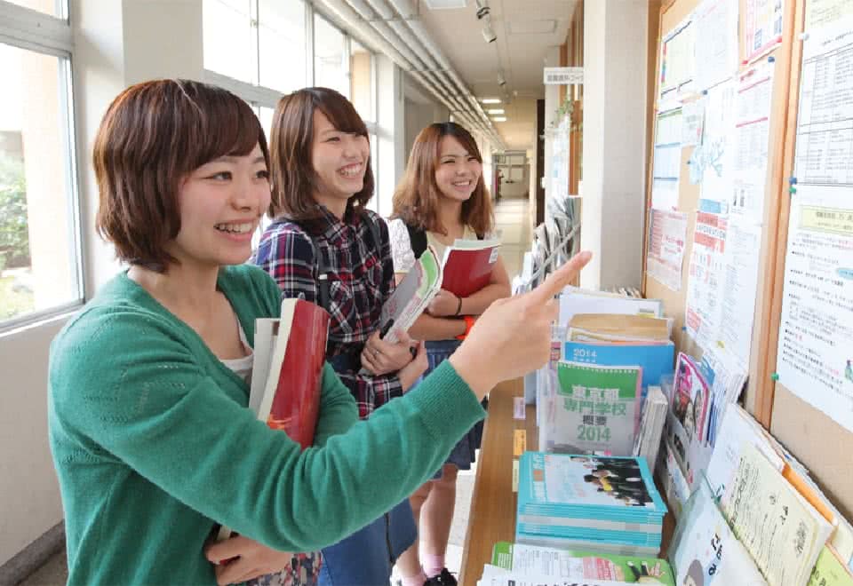 写真：廊下の掲示板に貼られた時間割を見ている3人の女子生徒