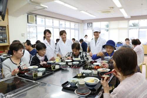 写真:ご飯を食べる地域の方と話す3名の学生