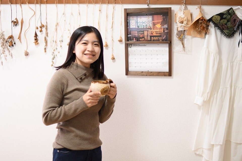 写真：マグカップを手にして、笑顔を向けるMさん