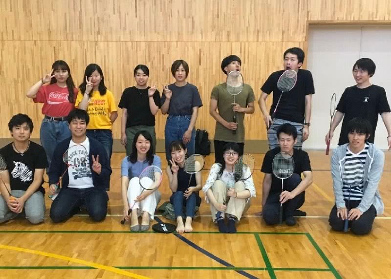 写真：体育館でラケットを持ったり、ポーズを取ったりして写真に収まるバドミントンサークルのメンバーたち