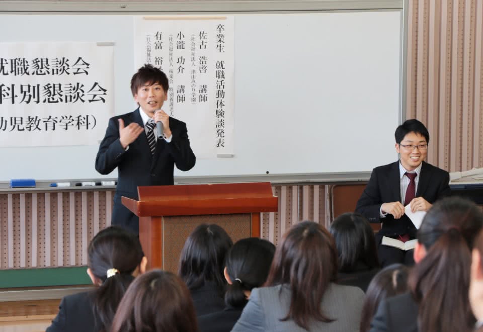 写真：卒業生の講話会の壇上で語る男子卒業生と、それを聞く学生たち