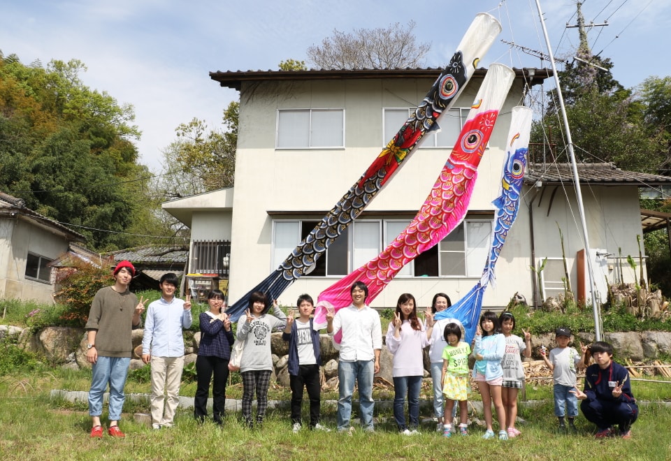 写真：じ・ば・子のおうちと鯉のぼりの前で記念撮影する子どもと高齢者、学生たち