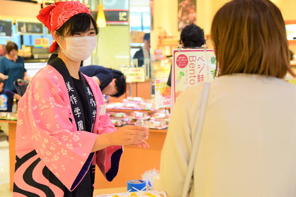 写真：マルイノースランド店にて実施した共同開発弁当販売キャンペーンでお客さんにアンケートに答えてもらう人見研究室の学生