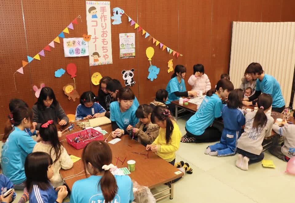 写真：地域のイベントで手作りおもちゃコーナーを開設する児童文化研究部と、そこで学生と一緒におもちゃを作る子どもたち