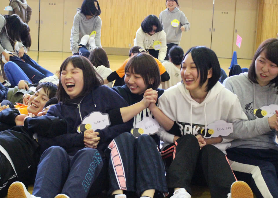 写真：体育館で手をつなぎあうレクリエーションを楽しむ学生たち